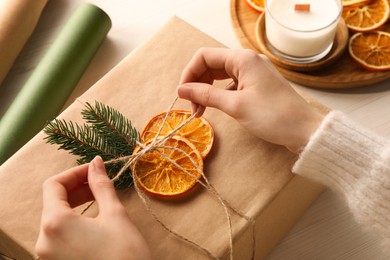 Photo of Woman decorating gift box with dry orange slices at white wooden table, closeup
