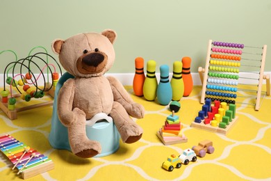 Photo of Teddy bear on light blue baby potty and many other toys indoors. Toilet training