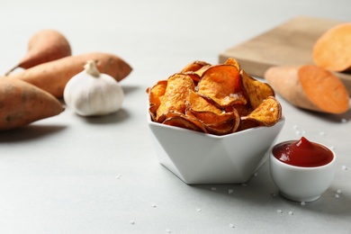 Delicious sweet potato chips in bowl and sauce on table. Space for text