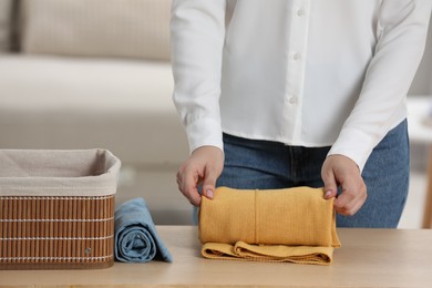 Photo of Woman rolling shirt at table indoors, closeup. Organizing clothes