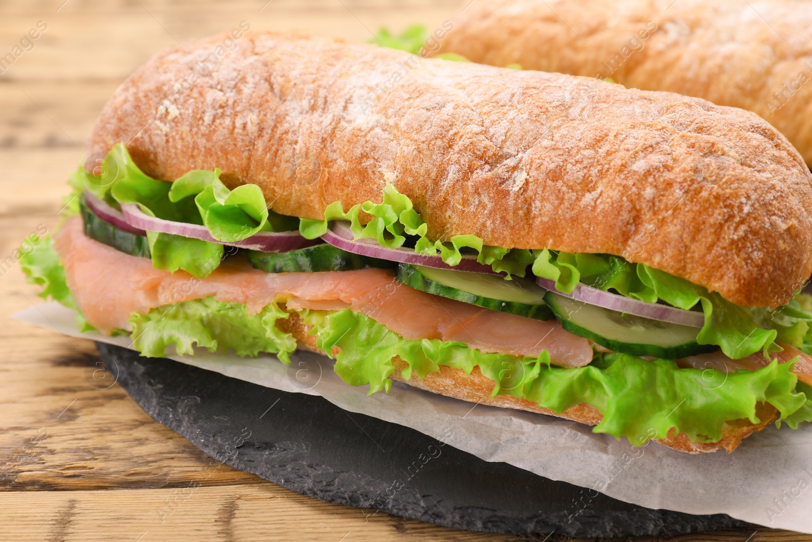 Photo of Delicious sandwich with fresh vegetables and salmon on wooden table, closeup