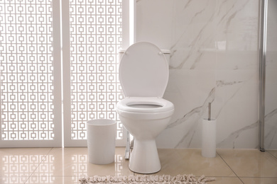 Photo of Modern white toilet bowl near marble wall indoors