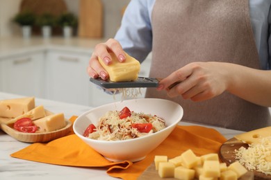 Woman grating cheese onto delicious pasta at white marble table in kitchen, closeup