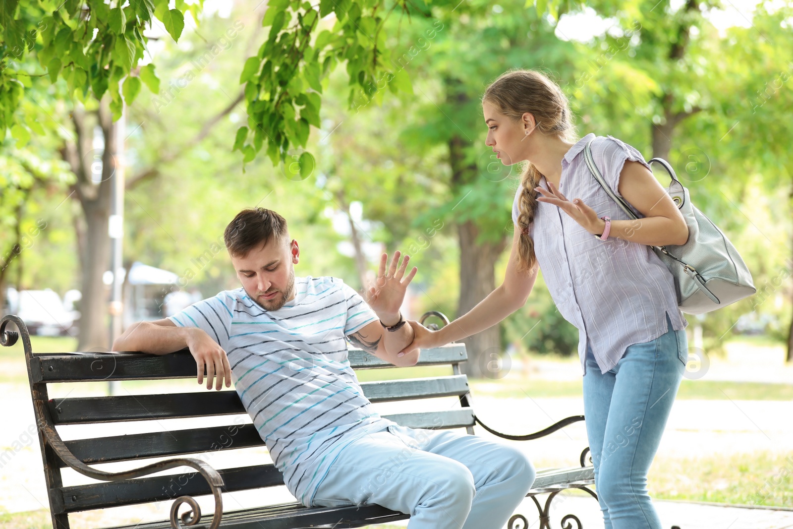 Photo of Young couple arguing while sitting on bench in park. Problems in relationship