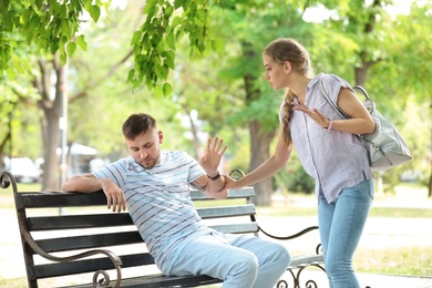 Young couple arguing while sitting on bench in park. Problems in relationship