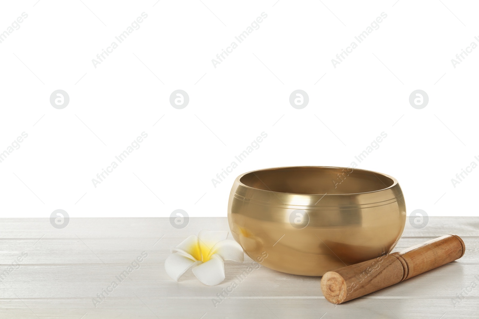 Photo of Golden singing bowl, mallet and flower on wooden table against white background, space for text