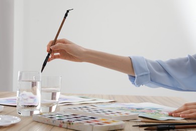 Photo of Woman painting flowers with watercolor at wooden table, closeup. Creative artwork