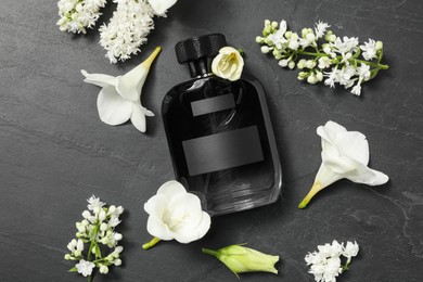 Bottle of luxury perfume and floral decor on black table, flat lay