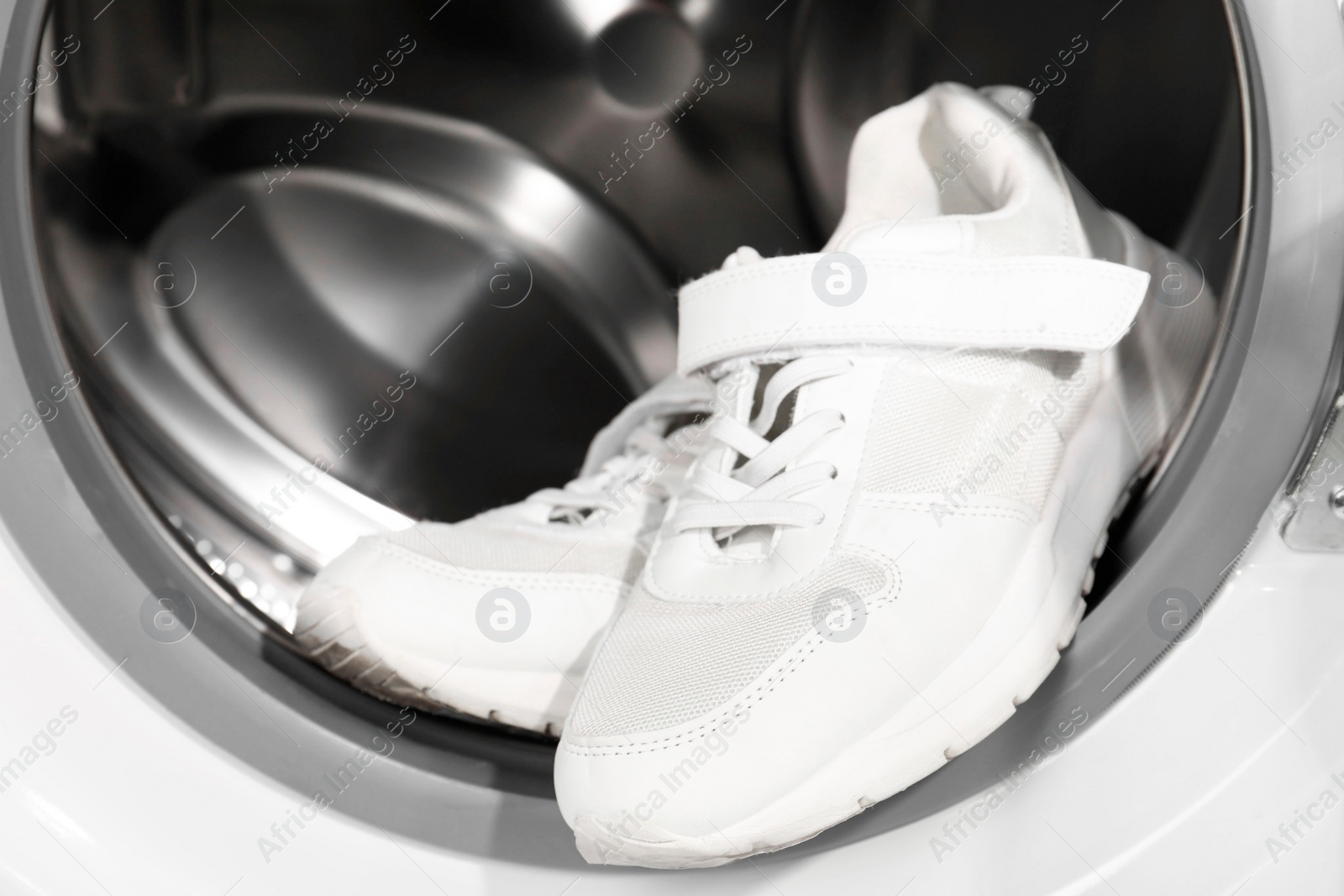 Photo of Stylish clean sneakers inside modern washing machine, closeup