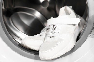 Photo of Stylish clean sneakers inside modern washing machine, closeup