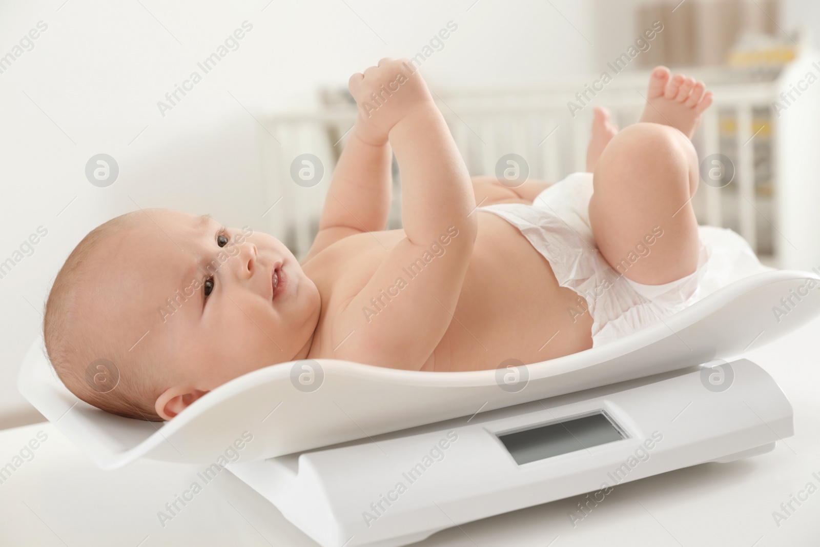 Photo of Cute little baby lying on scales in light room
