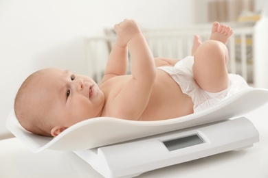Photo of Cute little baby lying on scales in light room