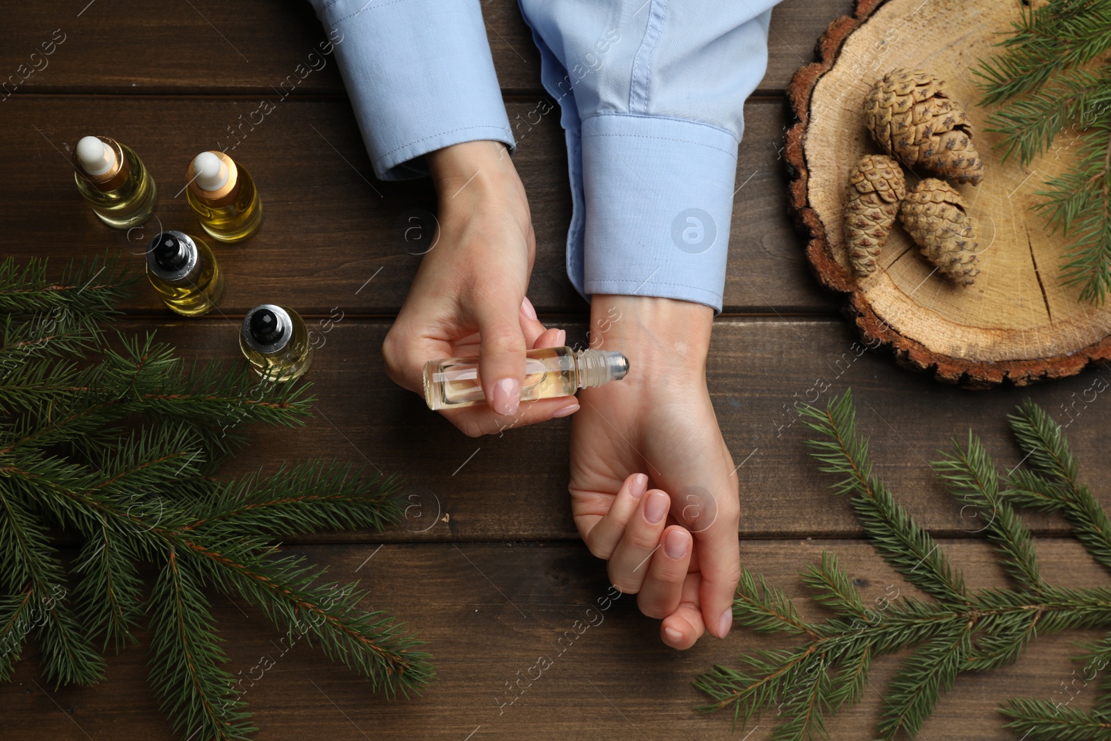 Photo of Woman applying pine essential oil on wrist at wooden table, top view