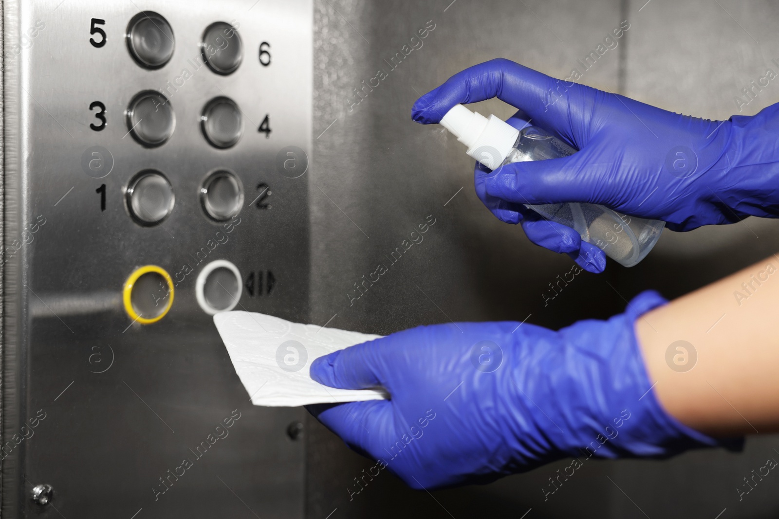 Photo of Woman with detergent spray and paper napkin cleaning elevator`s panel, closeup