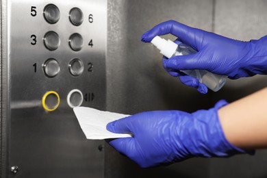 Photo of Woman with detergent spray and paper napkin cleaning elevator`s panel, closeup