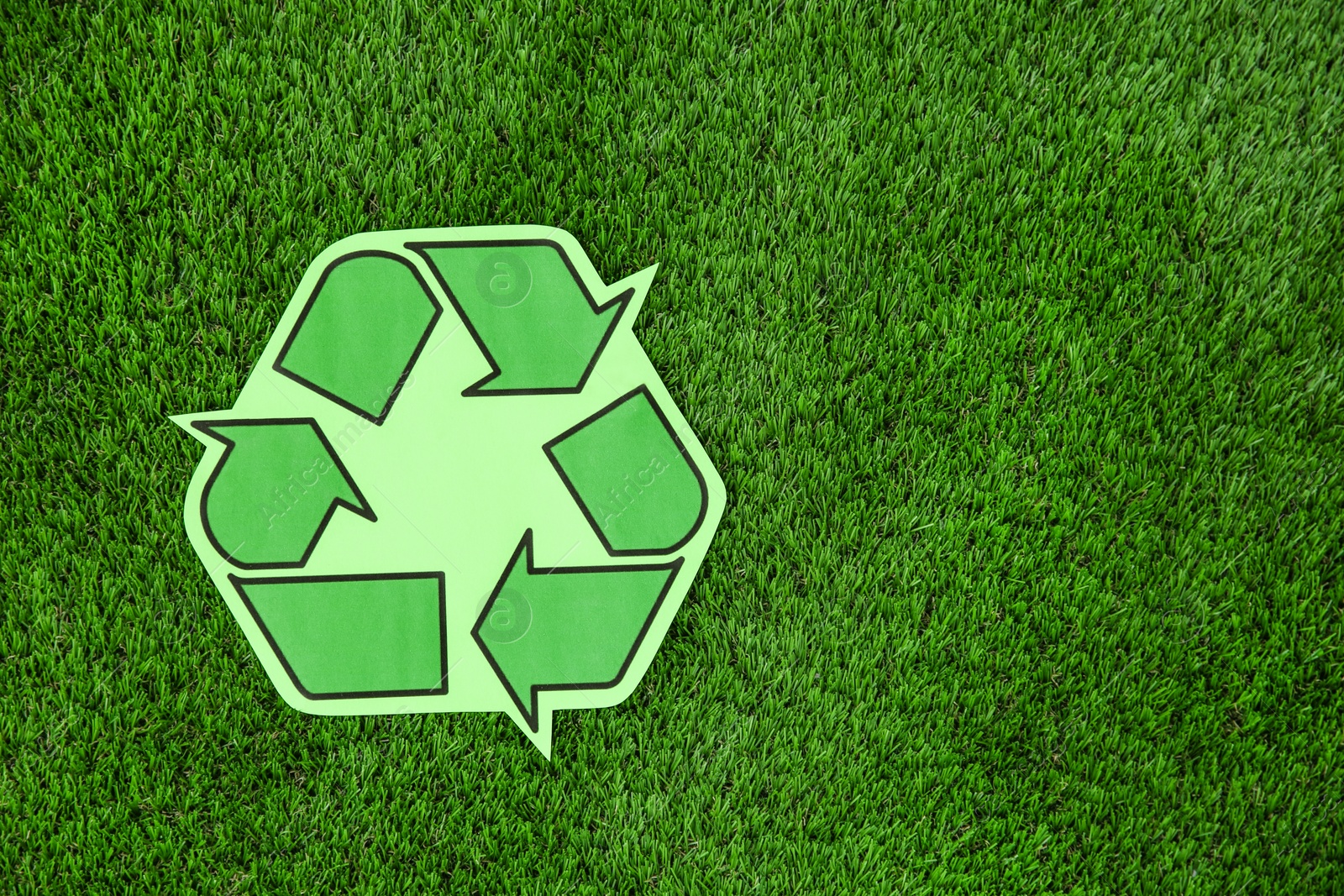 Photo of Paper recycling symbol on green grass, top view. Space for text