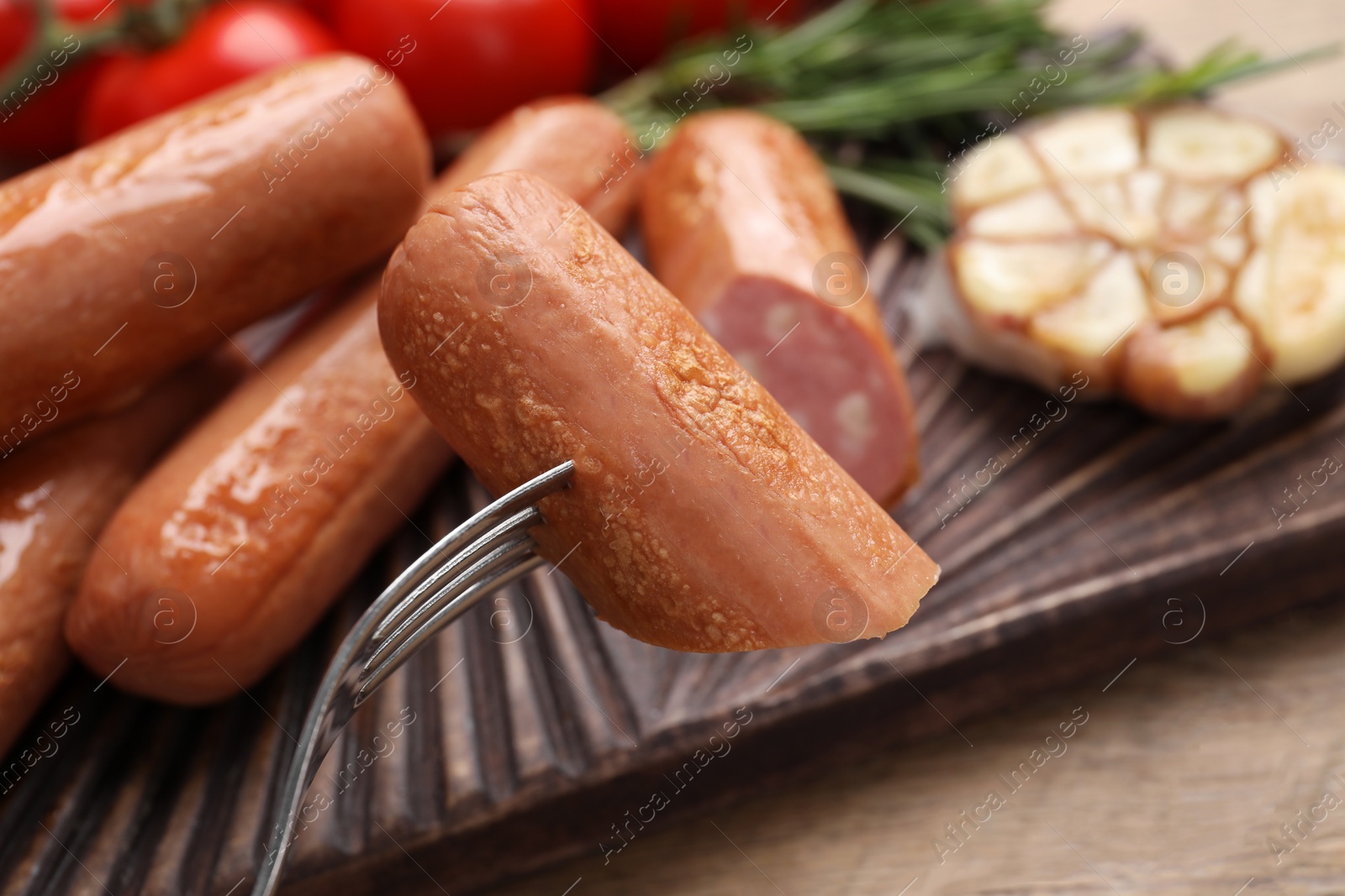 Photo of Delicious vegan sausage on fork over wooden table, closeup