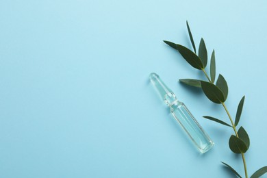 Photo of Medical ampoule with solution near eucalyptus on light blue background, flat lay. Space for text