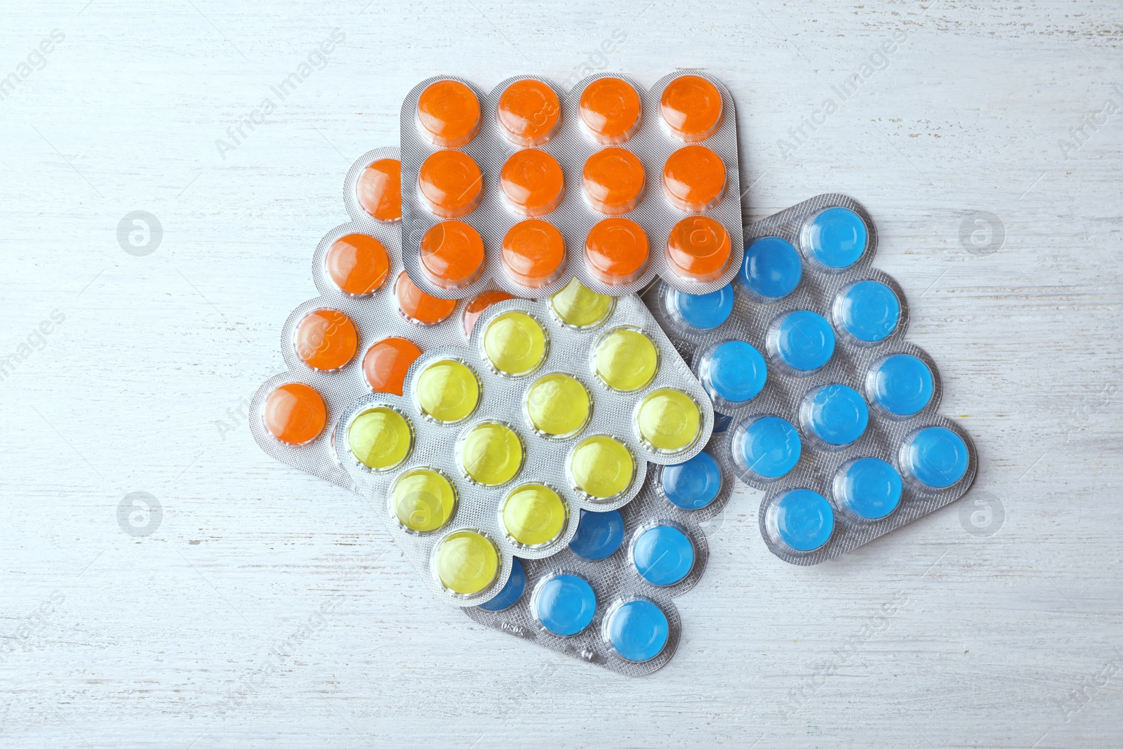 Photo of Blisters with color cough drops on white wooden table, top view