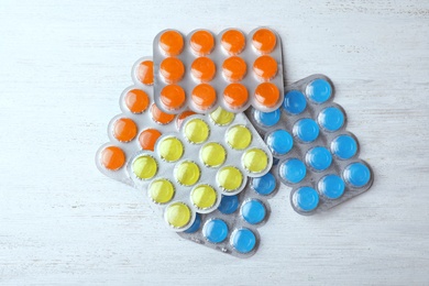 Blisters with color cough drops on white wooden table, top view