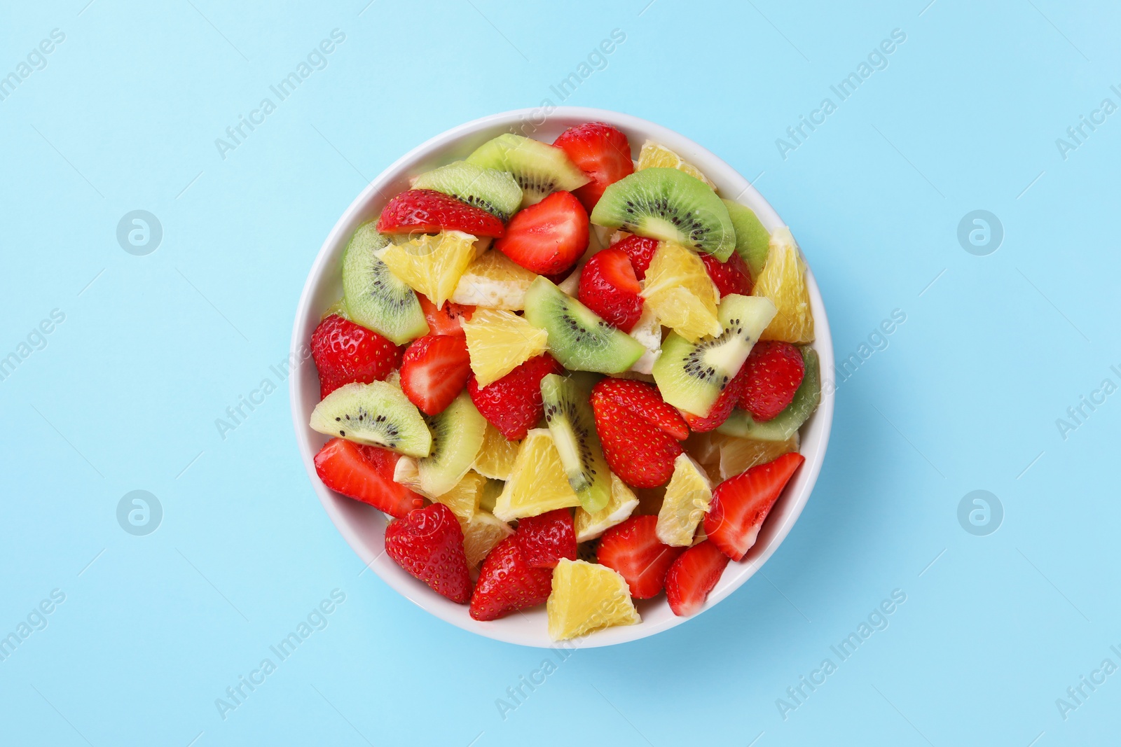 Photo of Yummy fruit salad in bowl on light blue background, top view