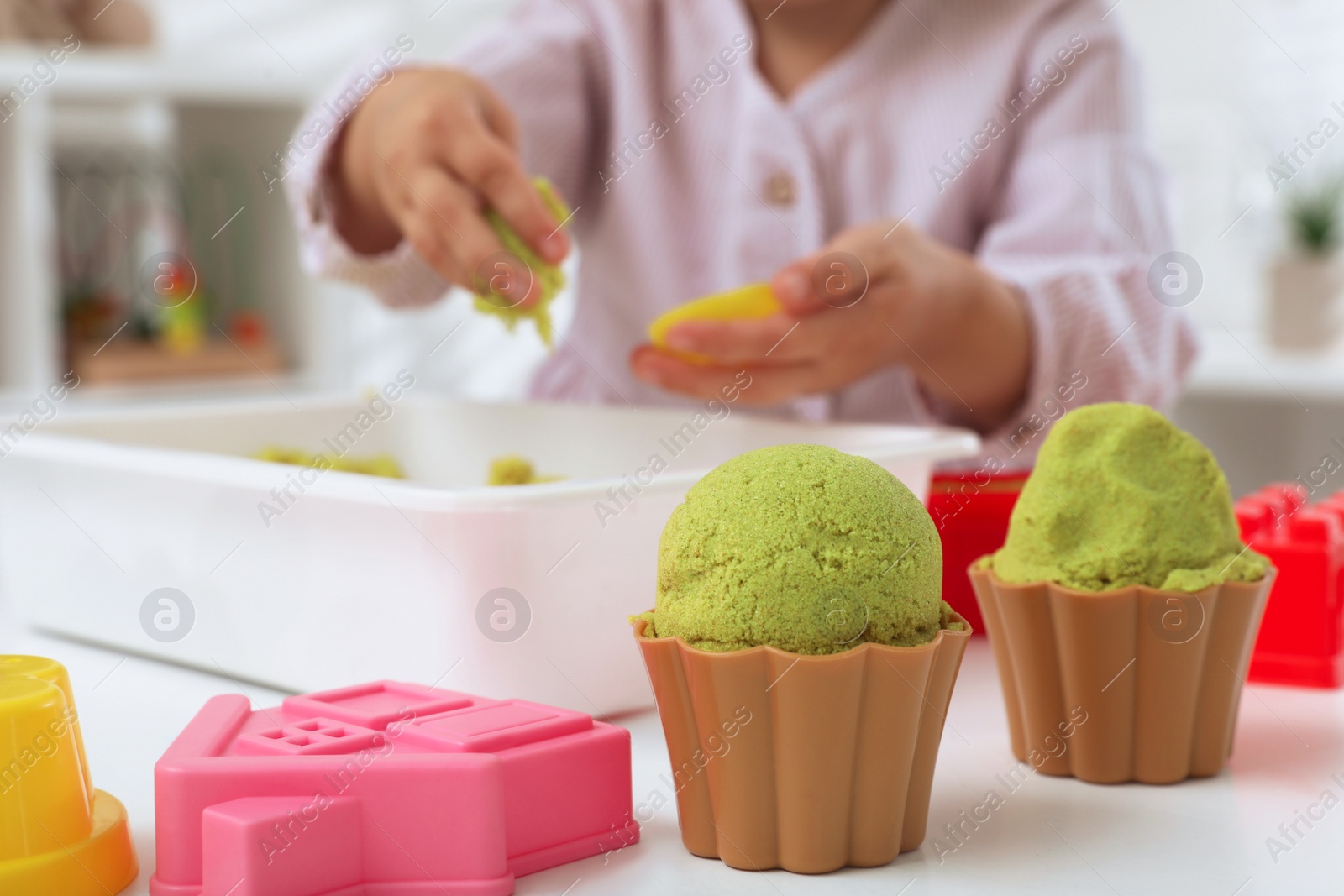 Photo of Little girl playing with bright kinetic sand at table indoors, focus on toys