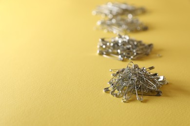 Photo of Piles of safety pins on yellow background, space for text