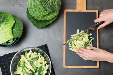 Woman cutting savoy cabbage on board at table, top view