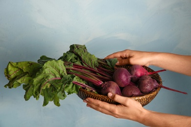 Young woman holding wicker basket with fresh beets on blue background, closeup