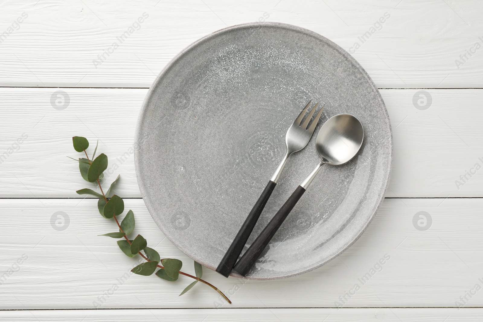 Photo of Stylish setting with cutlery, plate and eucalyptus branch on white wooden table, top view