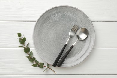Stylish setting with cutlery, plate and eucalyptus branch on white wooden table, top view