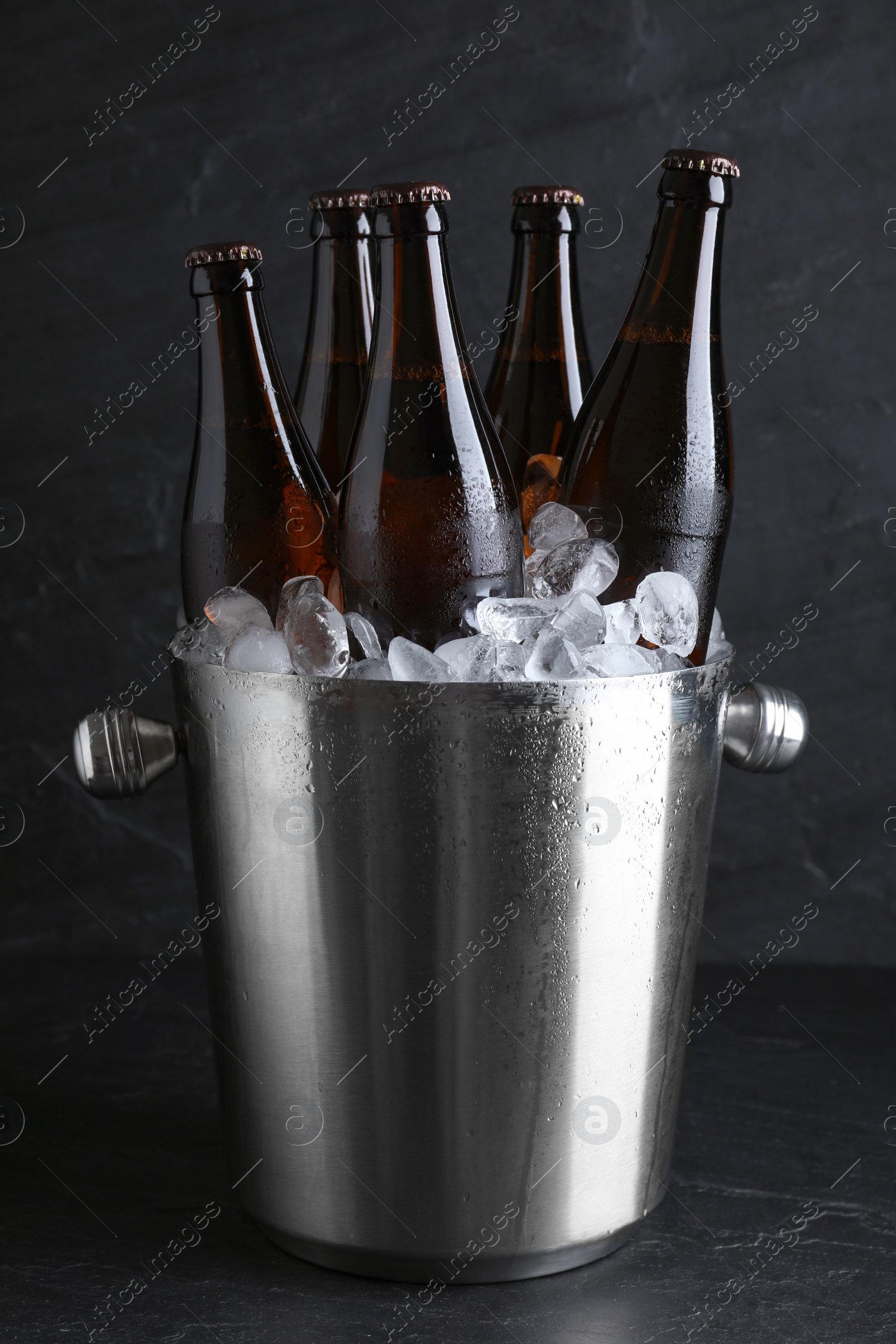 Photo of Metal bucket with beer and ice cubes on black table