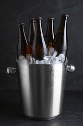 Metal bucket with beer and ice cubes on black table