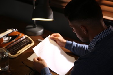 Photo of Man reading letter at wooden table in dark room