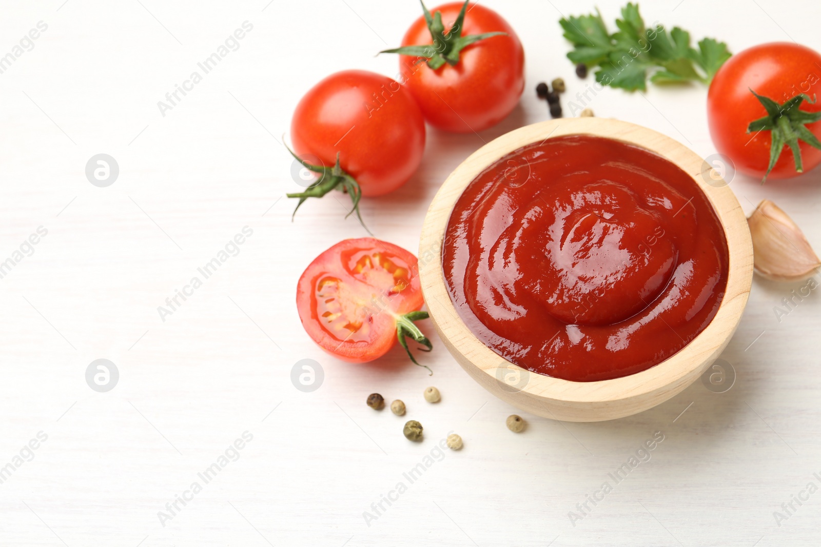 Photo of Delicious ketchup in bowl, peppercorns and tomatoes on white wooden table, above view. Space for text