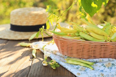 Photo of Wicker basket with fresh green beans on wooden table in garden