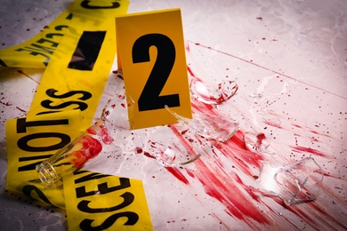 Yellow tape, crime scene marker and smithereens in blood on marble table, closeup