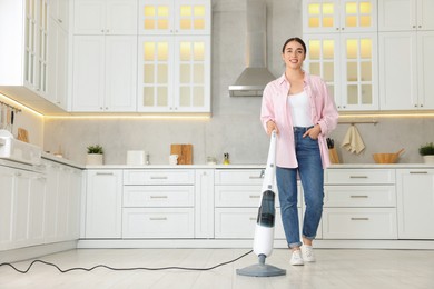 Happy woman cleaning floor with steam mop in kitchen at home. Space for text