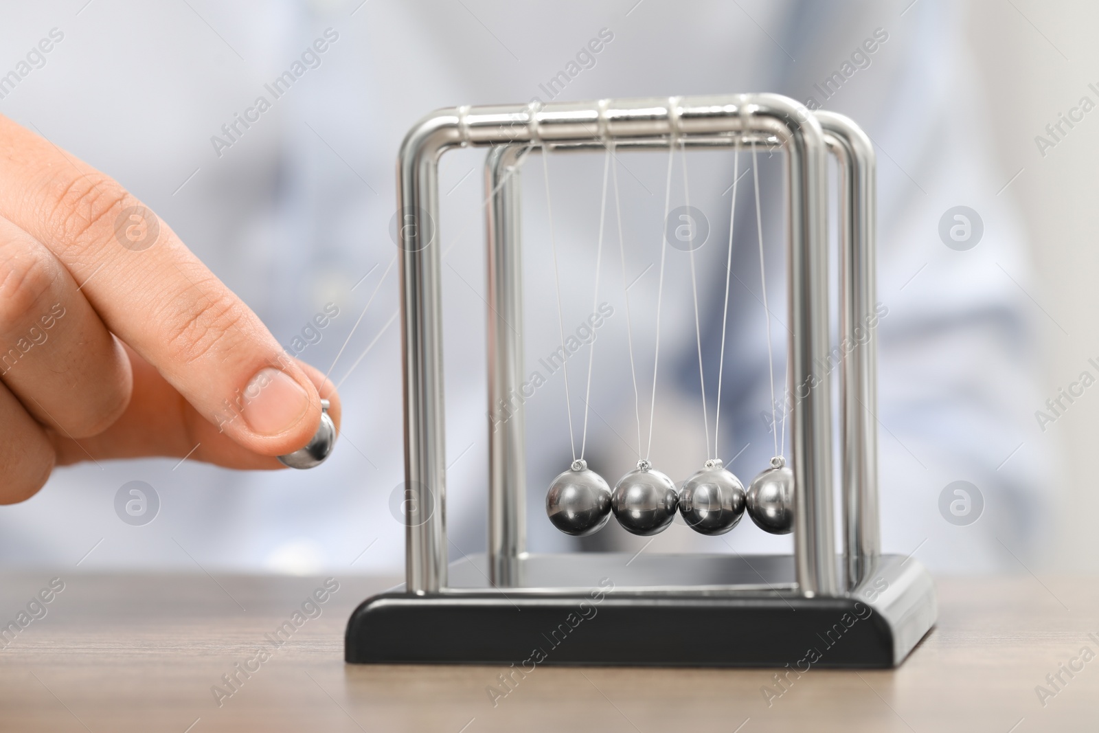 Photo of Man playing with Newton's cradle at table, closeup. Physics law of energy conservation