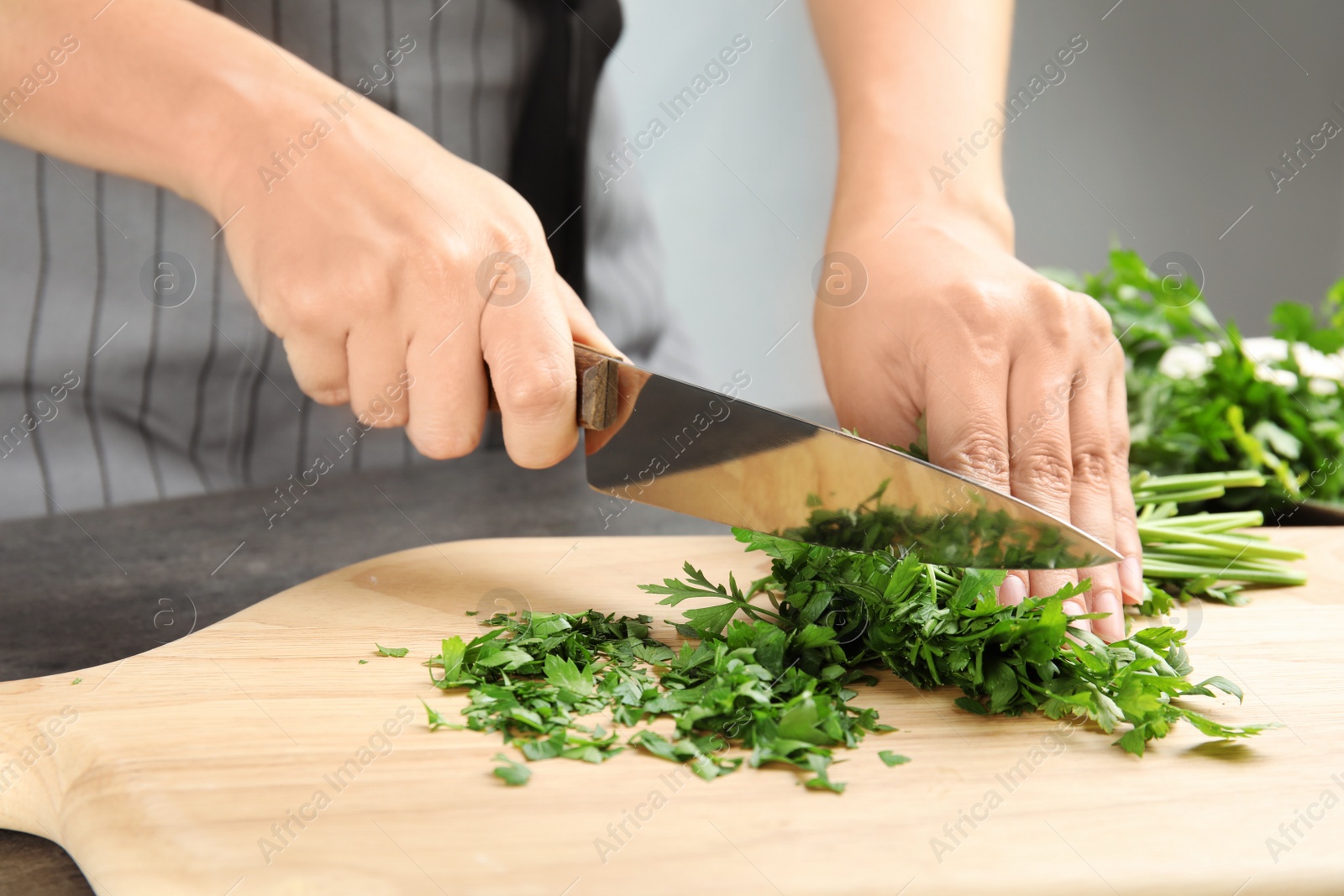 Photo of Woman cutting fresh green parsley on wooden board, closeup