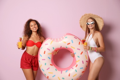 Photo of Beautiful young women in beachwear with cocktails and inflatable ring on color background