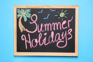 Photo of Chalkboard with phrase SUMMER HOLIDAYS on blue background, top view. School's out