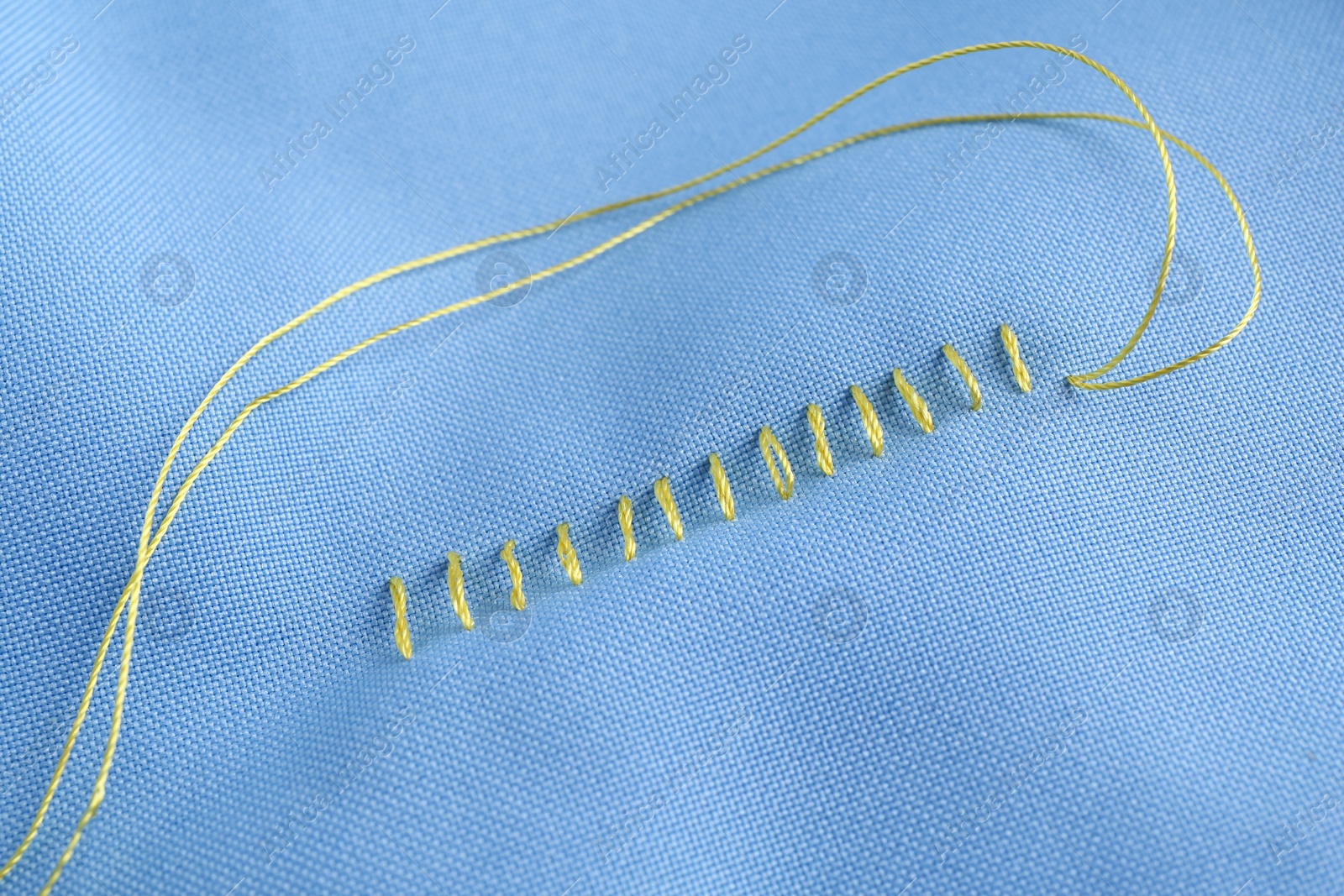 Photo of Sewing thread and stitches on light blue cloth, top view