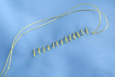Photo of Sewing thread and stitches on light blue cloth, top view