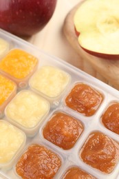 Photo of Different purees in ice cube tray and fresh apple fruits on wooden table, closeup. Ready for freezing