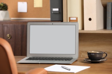 Photo of Modern laptop and cup on table in office