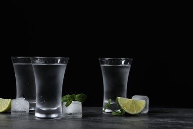 Photo of Shot glasses of vodka with lime slices, ice and mint on grey table
