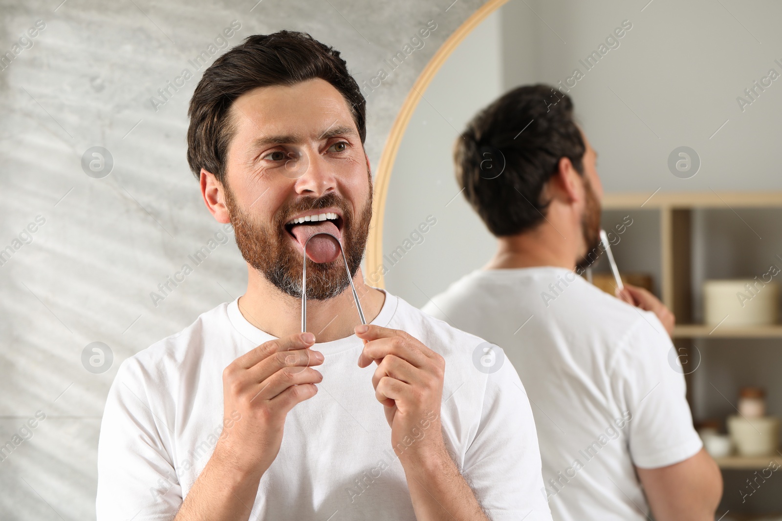 Photo of Handsome man brushing his tongue with cleaner in bathroom