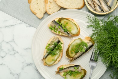 Photo of Delicious sandwiches with sprats, pickled cucumber, green onion and dill served on white marble table, flat lay. Space for text