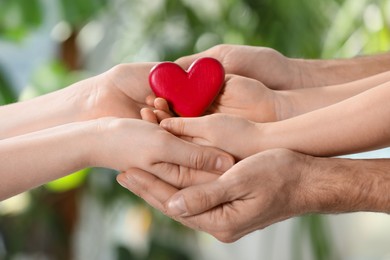 Parents and kid holding red heart in hands on blurred green background, closeup